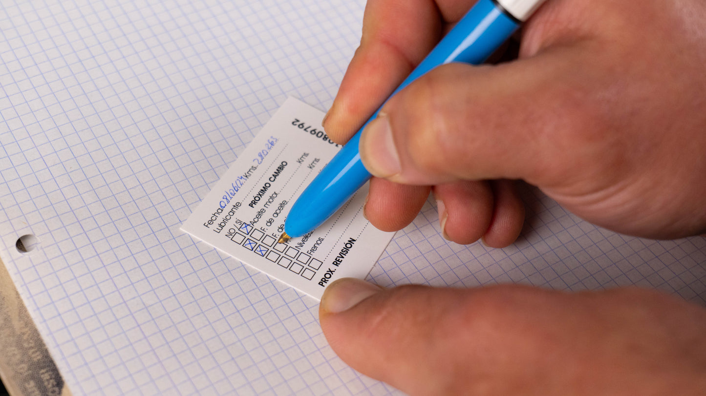 Manos rellenando la información en una etiqueta de mantenimiento Autosintético, detallando cambios de aceite, frenos y revisiones. Las pegatinas autoestáticas están diseñadas especialmente para talleres mecánicos.